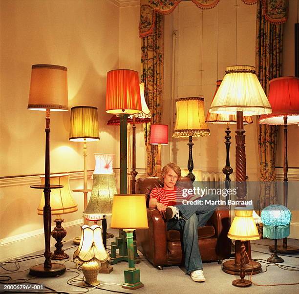 young man in armchair reading book, surrounded by lamps - lampada elettrica foto e immagini stock