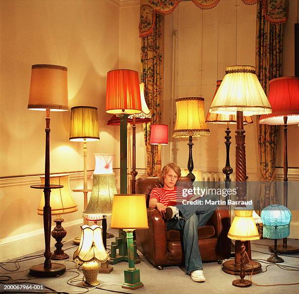 young man in armchair reading book, surrounded by lamps - lamp bildbanksfoton och bilder