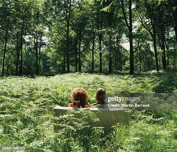 young couple on sofa in forest glade, rear view - couple forest stock-fotos und bilder