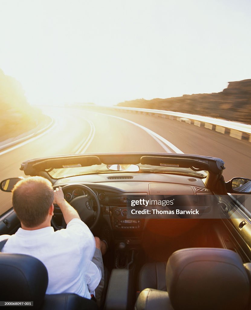 Man driving convertible car on highway, rear view