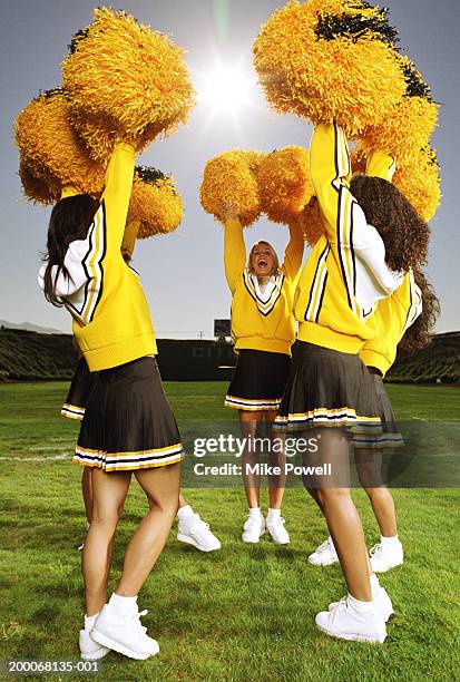 cheerleaders cheering on football field, shaking pompoms above heads - pom pom stock-fotos und bilder