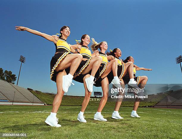 cheerleaders dancing arm and arm in formation, lifting knee, low angle - cheerleader photos fotografías e imágenes de stock