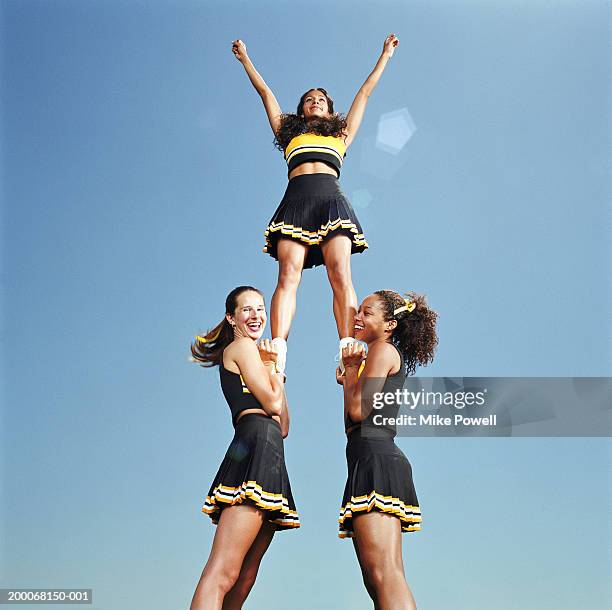 two cheerleaders lifting squad member in air, portrait, low angle - cheerleader photos fotografías e imágenes de stock