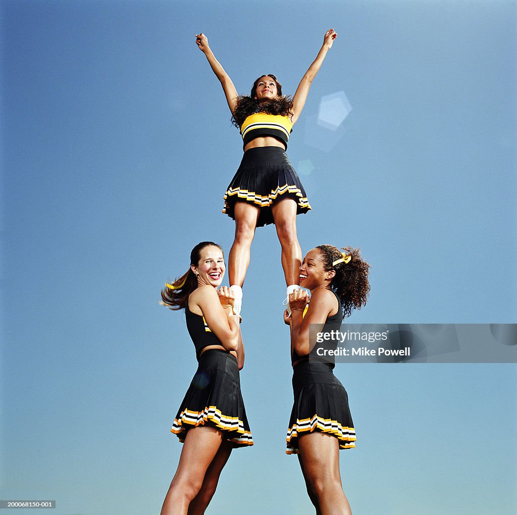 Two cheerleaders lifting squad member in air, portrait, low angle