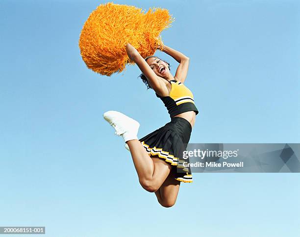 cheerleader jumping in mid air, holding pompoms, portrait - cheerleading stock-fotos und bilder