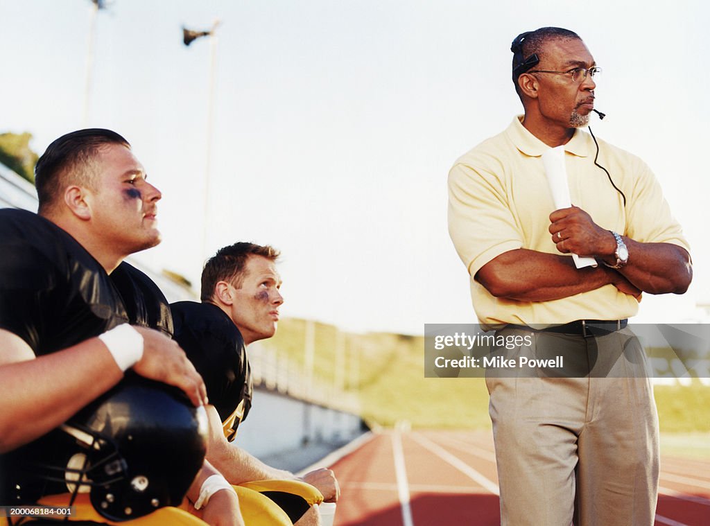 Football players with coach, watching game from side lines