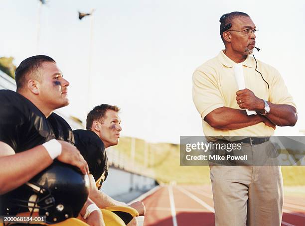 football players with coach, watching game from side lines - american football coach stock pictures, royalty-free photos & images