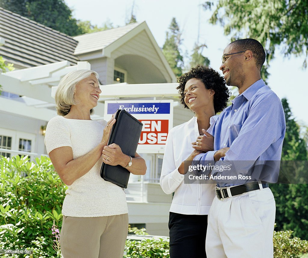 Mature woman standing with couple in front of Open House sign