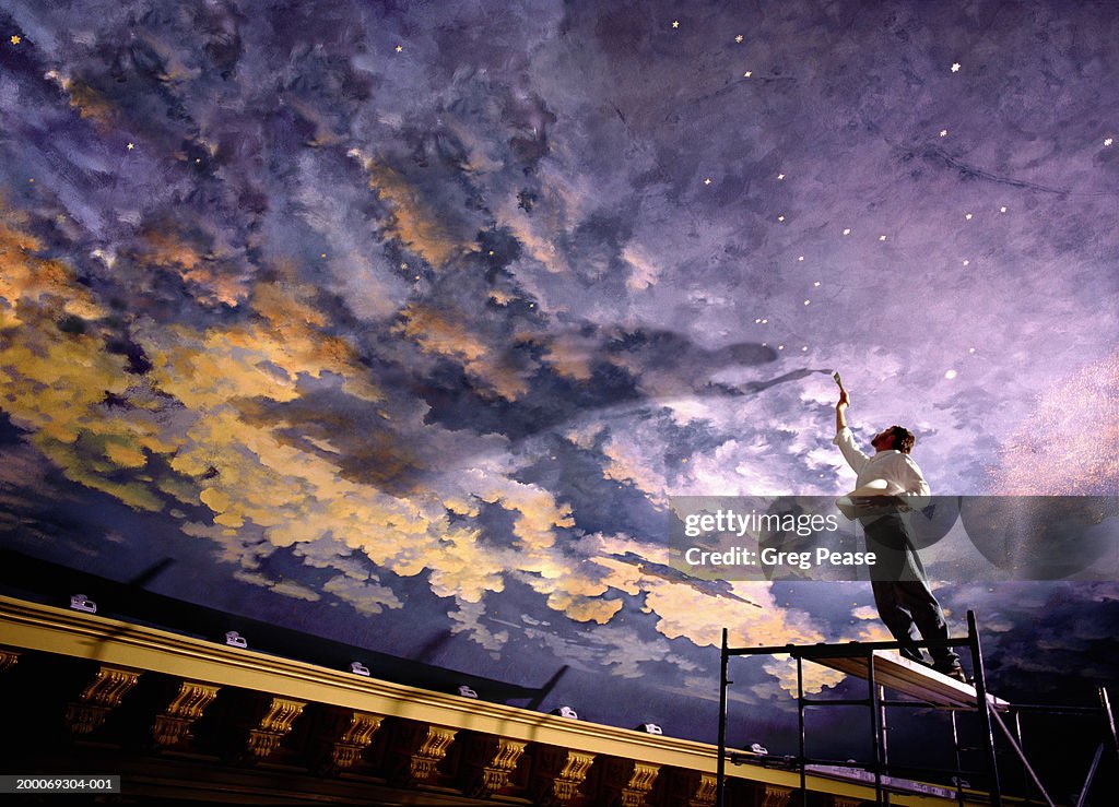 Man painting mural on ceiling, low angle view (digital composite)