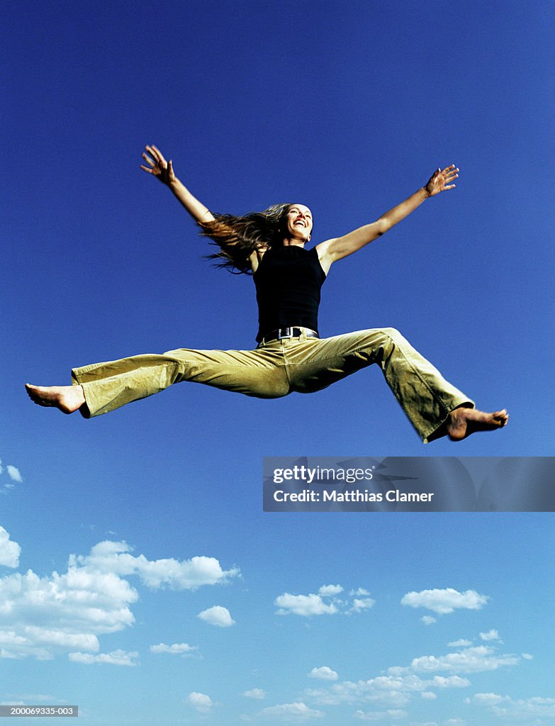 Woman jumping in mid air, arms and legs extended, low angle view