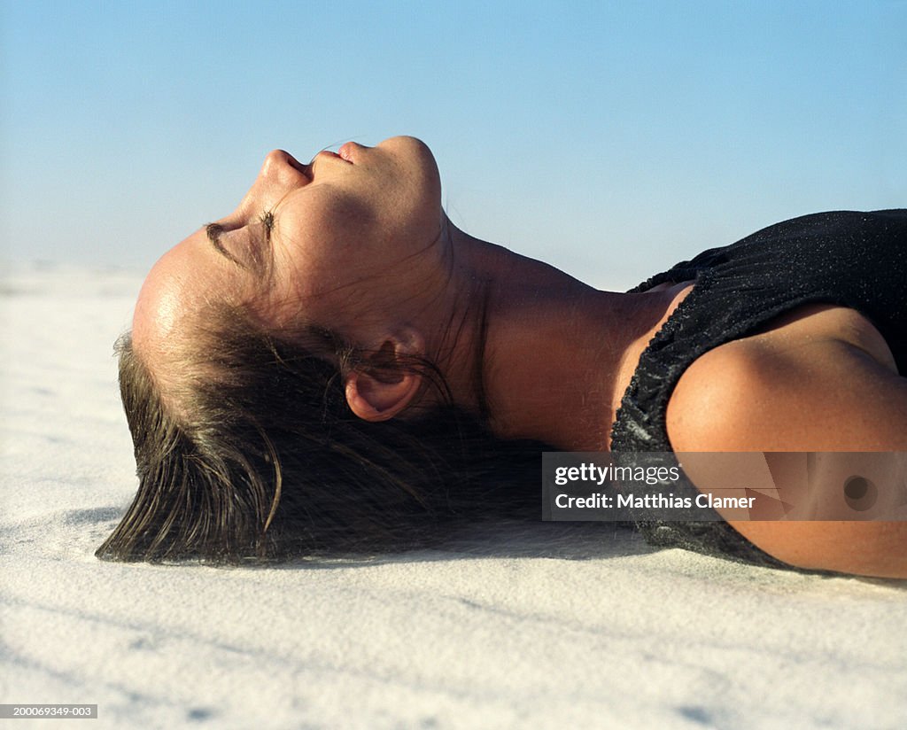 Woman with eyes closed lying in sand, side view