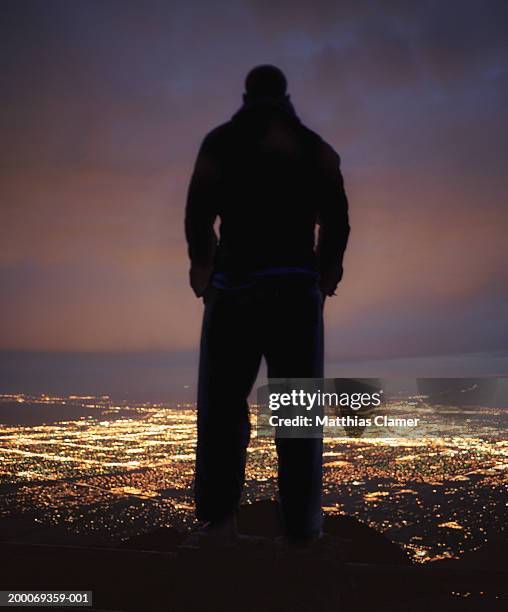 silhouette of man looking down on city at night, rear view - ominous stock-fotos und bilder