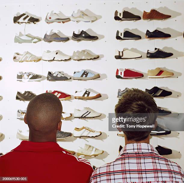 two teenage boys (15-17) looking at trainers in sports shop, rear view - schoenenwinkel stockfoto's en -beelden