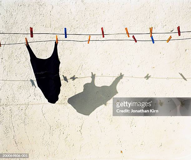swimsuit on clothesline casting shadow on stucco wall - badebekleidung stock-fotos und bilder