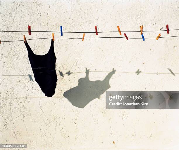 swimsuit on clothesline casting shadow on stucco wall - eendelig zwempak stockfoto's en -beelden