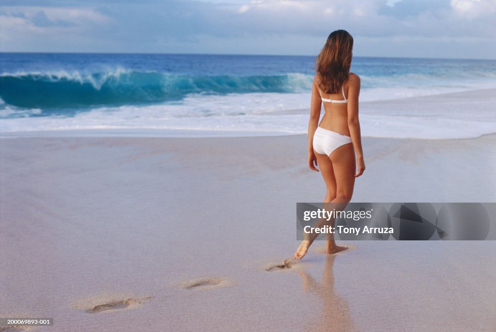 Young woman walking along beach, rear view