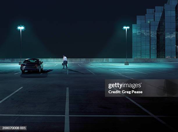 businessman walking toward car in empty parking lot at night - business man car stock-fotos und bilder