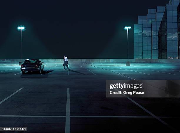 businessman walking toward car in empty parking lot at night - car park fotografías e imágenes de stock