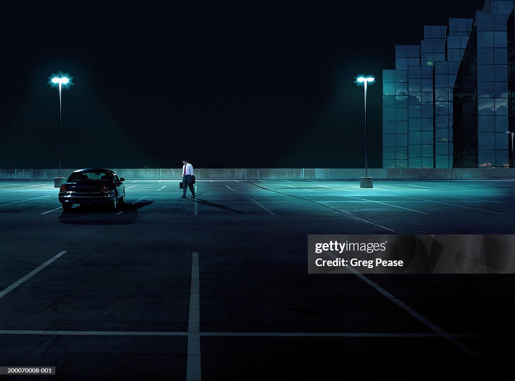 Businessman walking toward car in empty parking lot at night