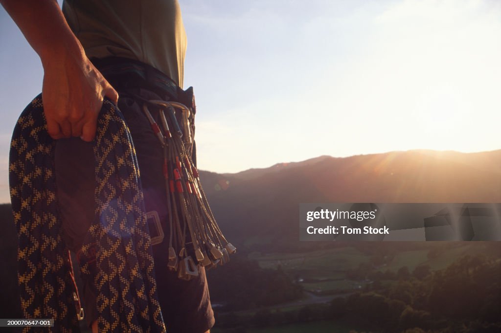 Male climber holding rope outdoors, sunset, mid section