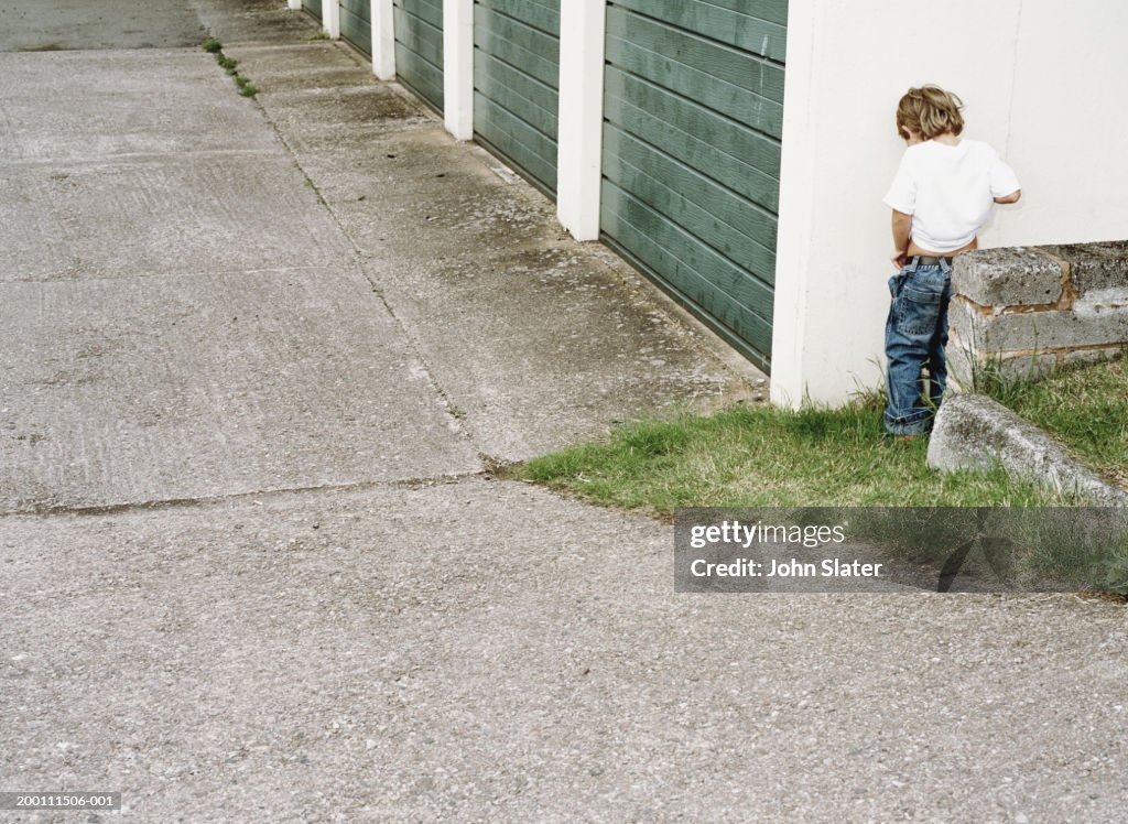 Boy (4-6) urinating against garage wall, rear view