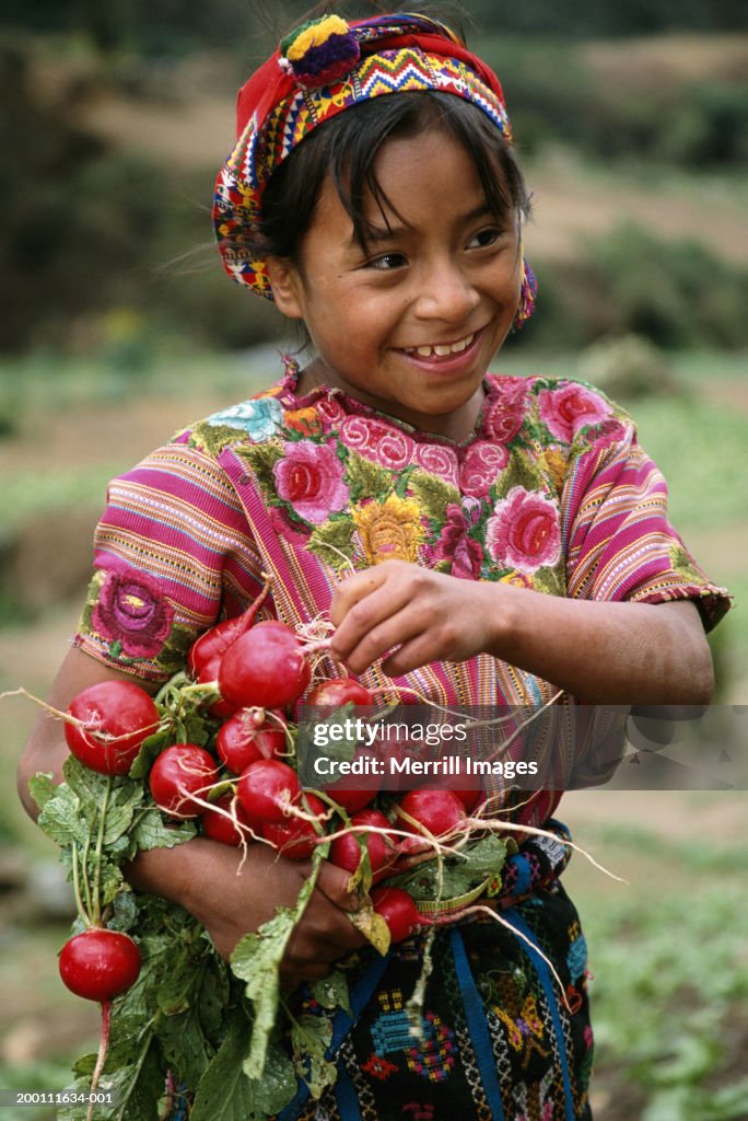 Girl (8-10) picking radishes, smiling
