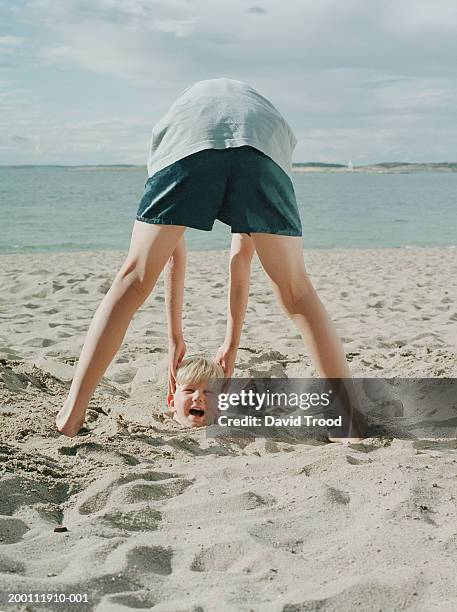 boy (10-12) holding head of boy (4-6) buried in sand, rear view - buried in sand stockfoto's en -beelden