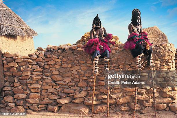 mali, dogon country, two male stilt dancers sitting on stone wall - dogon people stock pictures, royalty-free photos & images