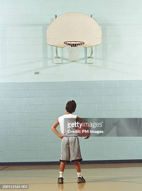 boy (8-10) holding basketball, looking at hoop, rear view - boyshorts fotografías e imágenes de stock