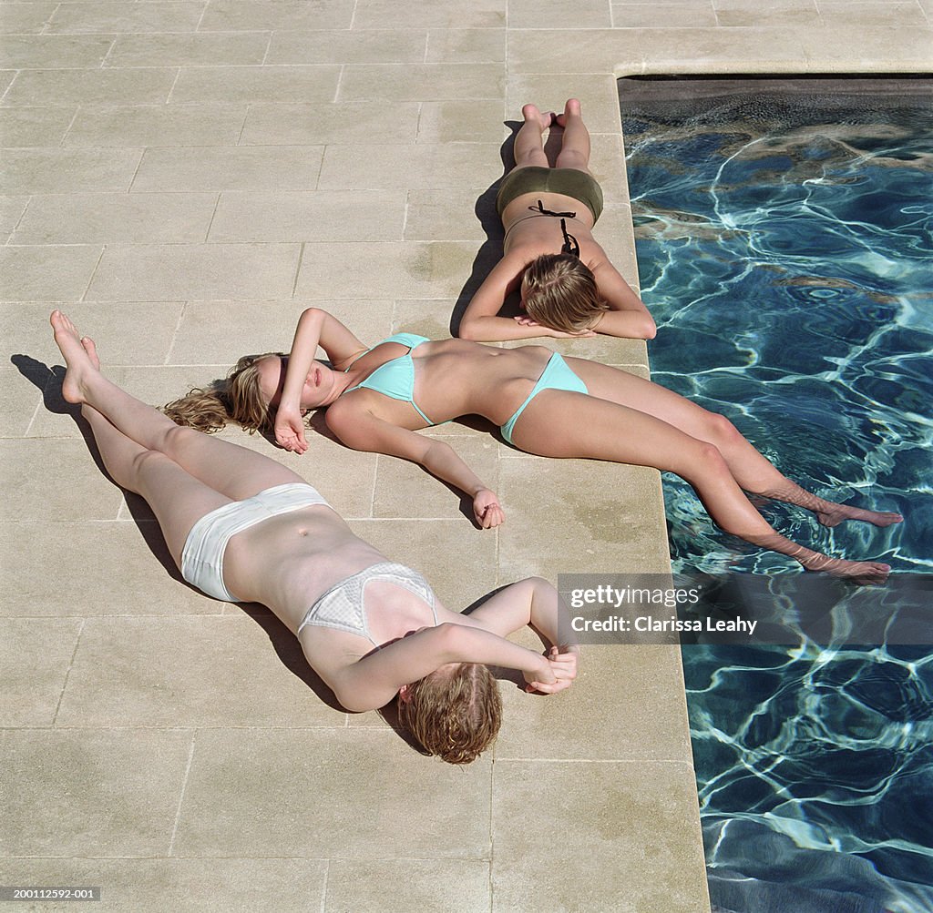 Three teenage girls (16-18) sunbathing by pool, elevated view