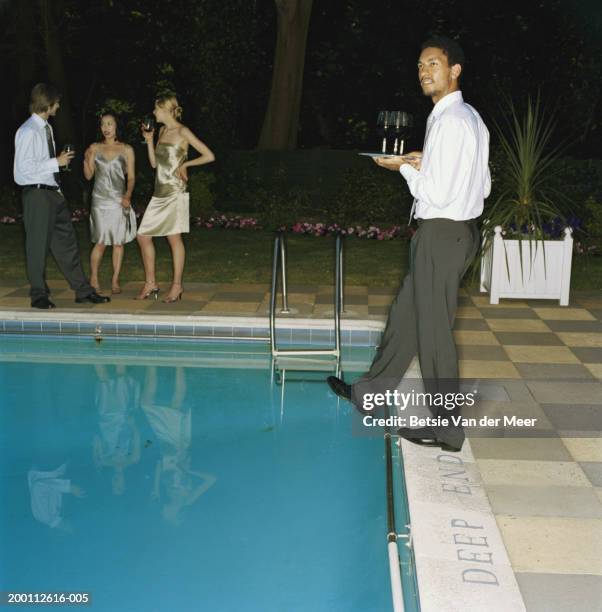 young man carrying tray of drinks, taking step at edge of outdoor pool - ignorance foto e immagini stock