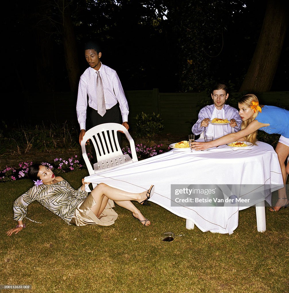 Four friends dining outdoors, woman falling, pulling cloth from table
