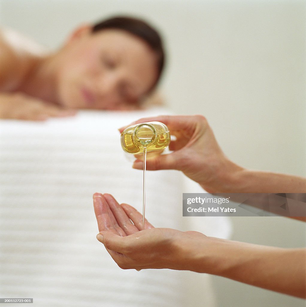 Woman pouring massage oil from bottle, focus on hand