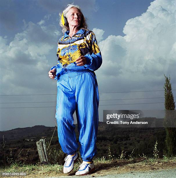 mature woman wearing head phones jogging on road - roupa de moleton - fotografias e filmes do acervo