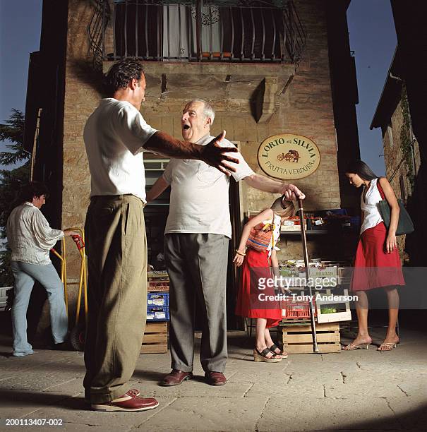 two mature men greeting each other at outdoor fruit stand - gesturing foto e immagini stock