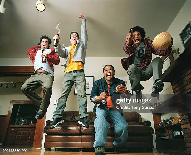 young men cheering and jumping in air in living room, low angle view - man cave stock-fotos und bilder