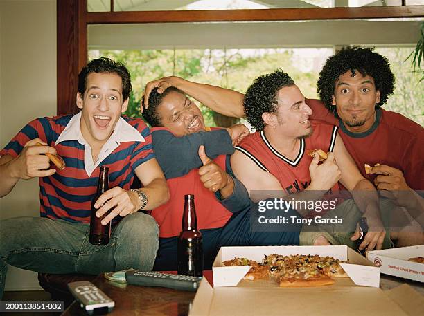 young men sitting in living room watching game and eating pizza - four people foto e immagini stock
