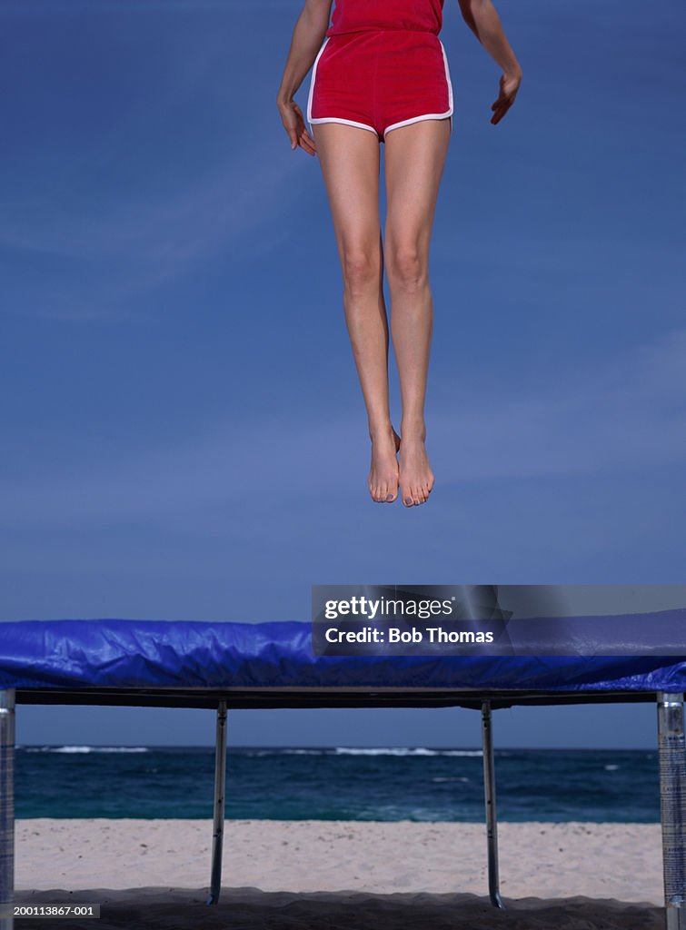 Young woman jumping on trampoline, low section