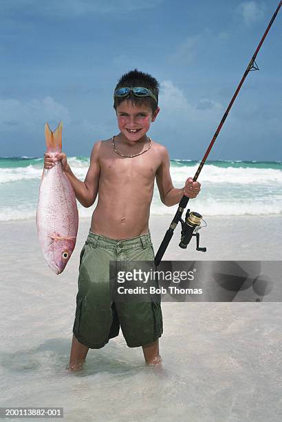boy (5-7) holding fishing rod and fish on beach, portrait - fish barbados stock pictures, royalty-free photos & images