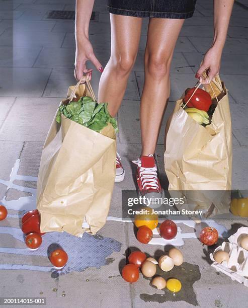 woman holding split bags, groceries spilling on floor, low section - high and low stockfoto's en -beelden