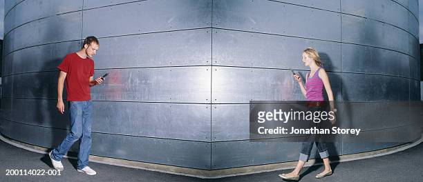 young man and woman walking toward each other staring at mobile phones - zusammenprall stock-fotos und bilder