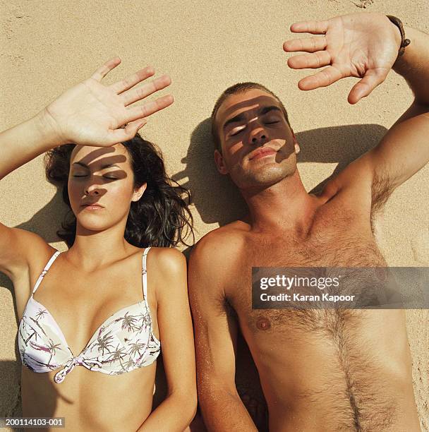 young couple lying on beach shielding faces from sun, elevated view - chest hair stock pictures, royalty-free photos & images