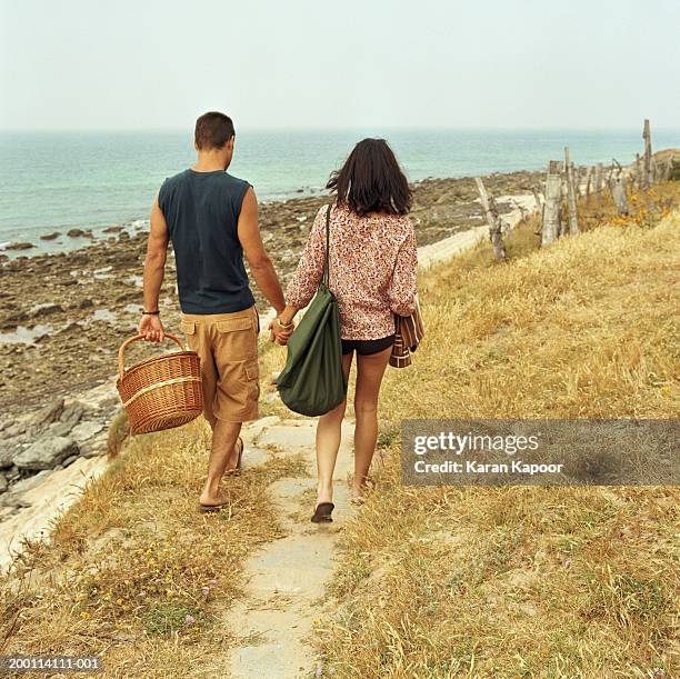 young couple hand in hand, man carrying picnic basket, rear view - paar picknick stock-fotos und bilder