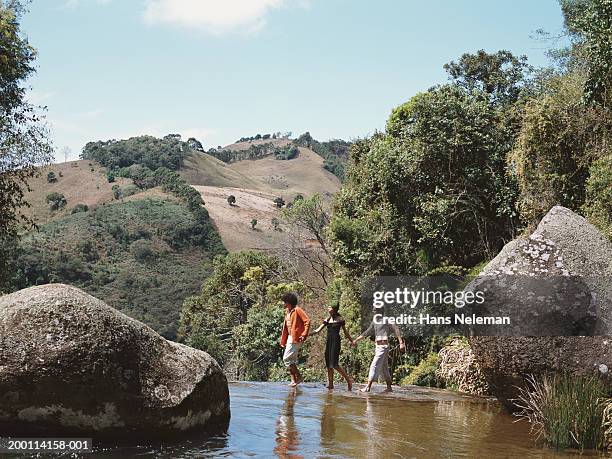 two men and one woman holding hands, walking across stream - hands in her pants fotografías e imágenes de stock