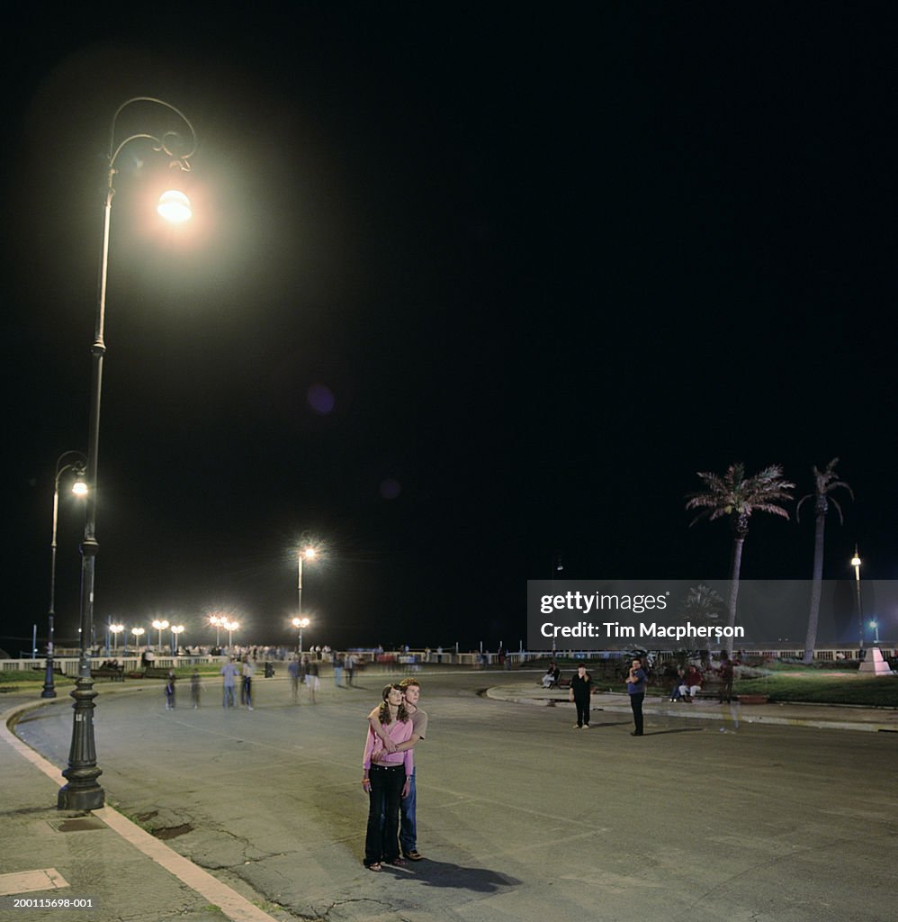 Young couple in road, man embracing woman, night