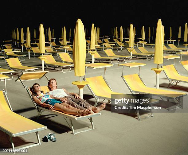 young couple on beach sharing sun lounger, night - casual couple photos et images de collection