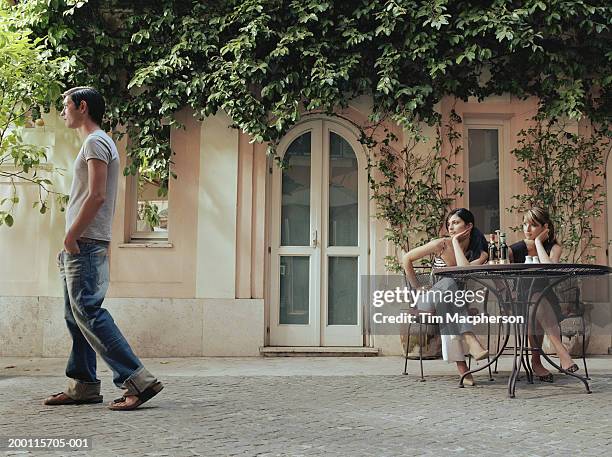 two young women at cafe table watching man walk by - maschio con gruppo di femmine foto e immagini stock