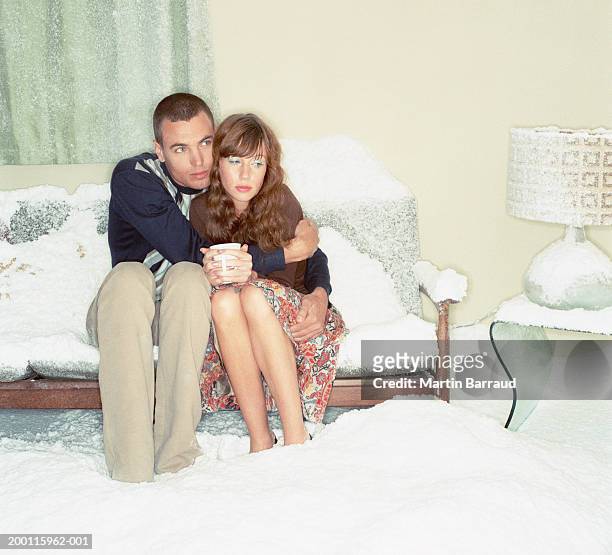couple embracing on sofa in snow-filled room - froid photos et images de collection