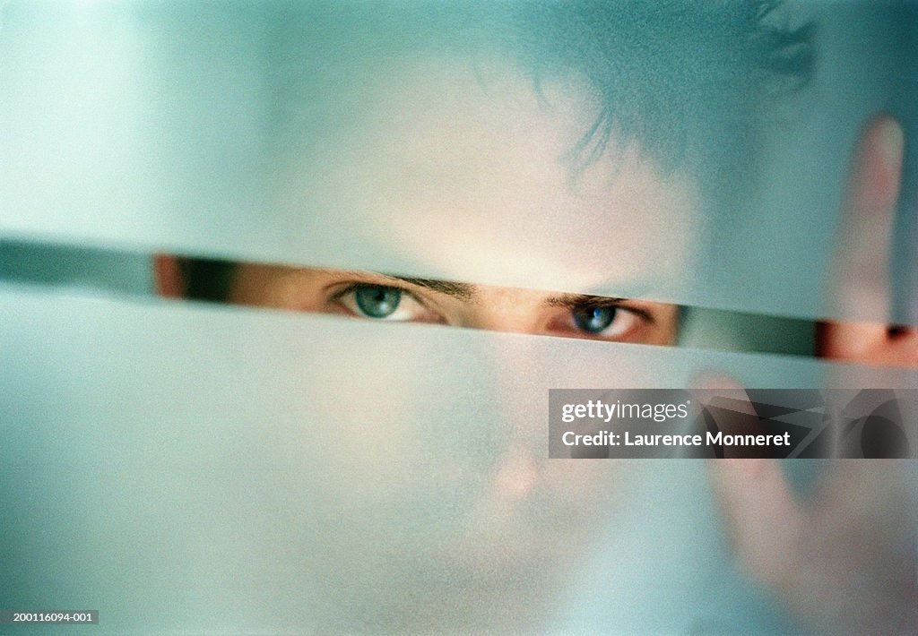 Man peering through gap in frosted glass, portrait, close-up