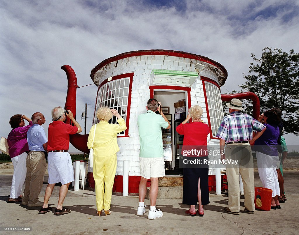 Group of mature adults photographing teapot-shaped hut, rear view